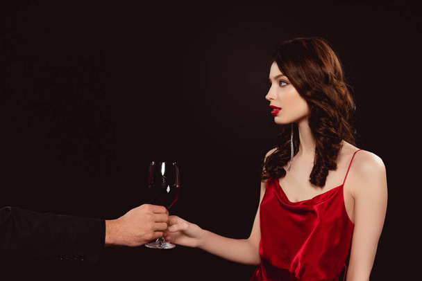 Side view of man giving glass of red wine to elegant girl isolated on black - Foto, imagen