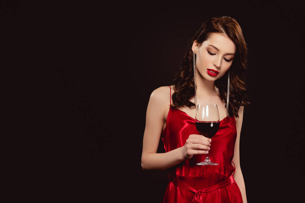 Elegant woman in red dress holding glass of wine isolated on black - Zdjęcie, obraz