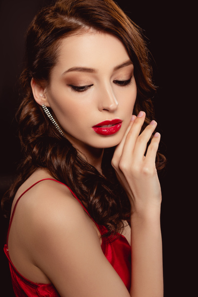 Side view of attractive brunette woman with red lips and hand near face isolated on black - Zdjęcie, obraz