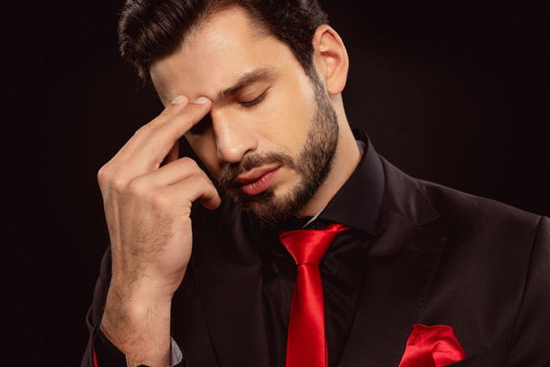 Hombre pensativo en traje y corbata roja con dedos cerca de la frente aislados en negro
 - Foto, imagen