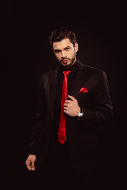 Elegant man in black suit and red tie looking at camera isolated on black - 写真・画像
