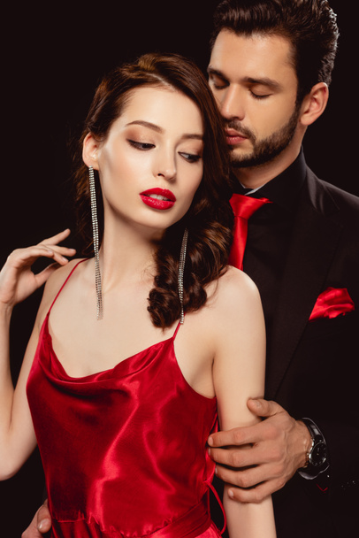 Elegant man embracing beautiful woman in red dress isolated on black - Photo, Image