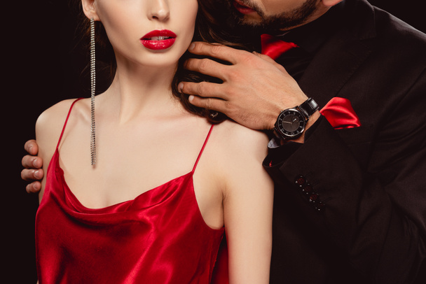 Обрезанный вид элегантного мужчины трогательные волосы подруги в красном платье изолированы на черном
 - Фото, изображение