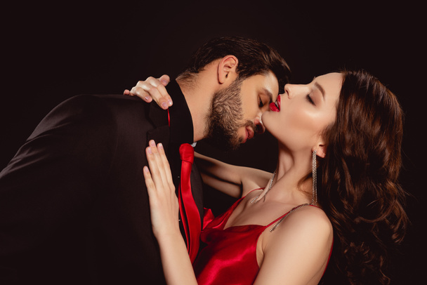 Vista lateral do homem bonito beijando namorada elegante com lábios vermelhos isolados no preto
 - Foto, Imagem