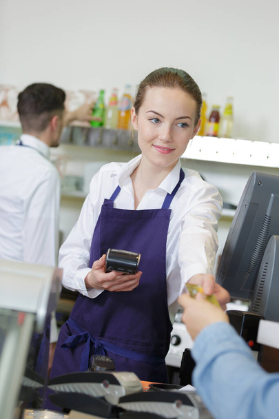 smiling young waitress processing a customer payment - Fotó, kép