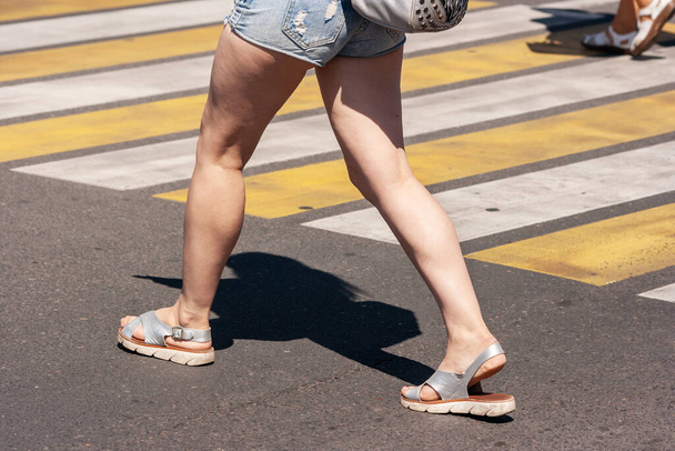 kobieta przechodząca przez ulicę na przejściu w mieście w letni dzień. zbliżenie nóg - Zdjęcie, obraz
