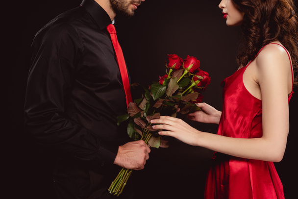 Cropped view of man giving bouquet of roses to elegant woman isolated on black - Photo, Image