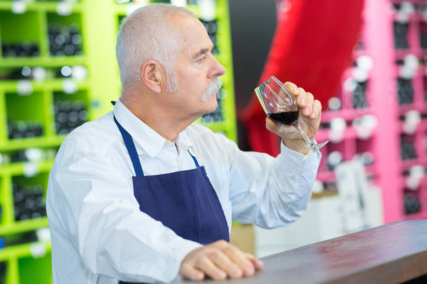 elderly seller tasting wine at store - Foto, afbeelding