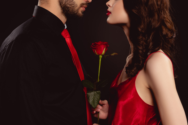 Cropped view of elegant woman holding rose near boyfriend isolated on black - Фото, изображение