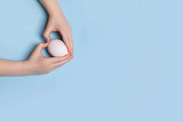 White chicken egg in the hands of a child on a blue background - Foto, Bild