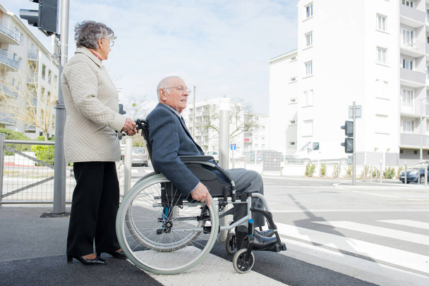 pareja de ancianos en silla de ruedas cruzando la carretera
 - Foto, imagen