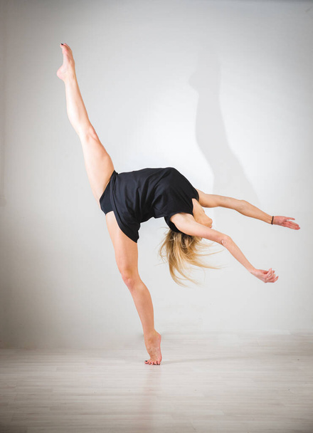 Young professional gymnast in black sportswear looks straight, stretches palms towards camera, bottom shot, rhythmic gymnastics concept - Photo, image