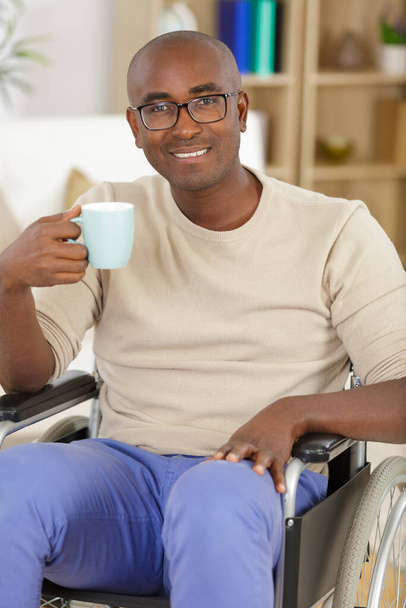 mature man in wheelchair drinking coffee indoors - Foto, imagen