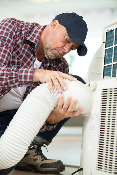 Mužský dělník rozhoduje o pružném ventilačním potrubí v dílně - Fotografie, Obrázek