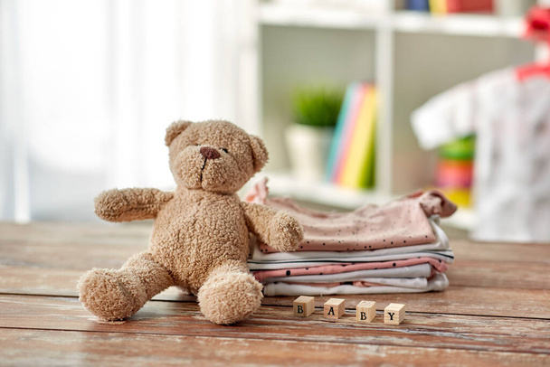baby clothes and teddy bear toy on table at home - Fotoğraf, Görsel