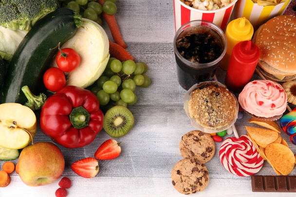 υγιεινά ή ανθυγιεινά τρόφιμα. Concept φωτογραφία των υγιεινών και ανθυγιεινών τροφίμων. Φρούτα και λαχανικά vs ντόνατς, γλυκά και μπιφτέκια στο τραπέζι - Φωτογραφία, εικόνα