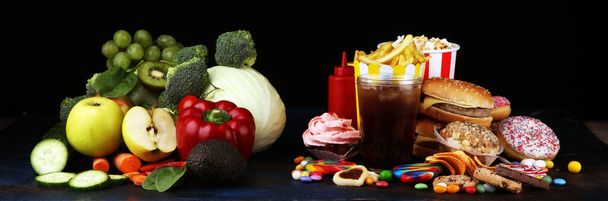 gesunde oder ungesunde Nahrung. Konzeptfoto von gesunder und ungesunder Ernährung. Obst und Gemüse gegen Donuts, Bonbons und Burger auf dem Tisch - Foto, Bild