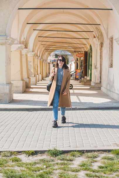nuori melko muodikas nainen kävelee ruskea takki kaupungin kadulla
 - Valokuva, kuva