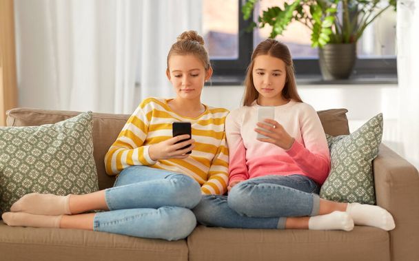 girls with smartphones sitting on sofa at home - Φωτογραφία, εικόνα