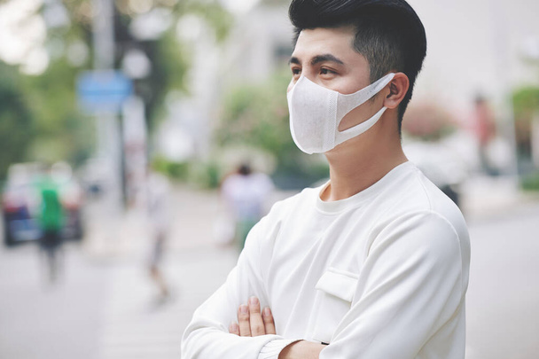 Bello giovane uomo in piedi all'aperto indossando maschera medica per proteggere gli altri dalla diffusione del virus - Foto, immagini