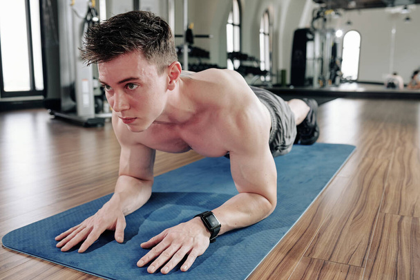 Красивый сильный молодой человек тренируется в помещении и делает упражнения на доске в спортзале
 - Фото, изображение