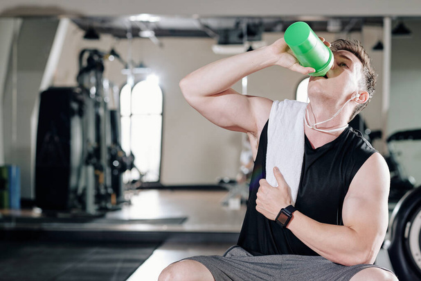 Durstiger junger Bodybuilder trinkt nach anstrengendem Training im Fitnessstudio Vitaminwasser - Foto, Bild