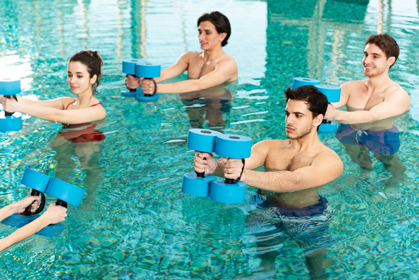 Grupa młodych ludzi ćwiczących ze sztangami w basenie - Zdjęcie, obraz