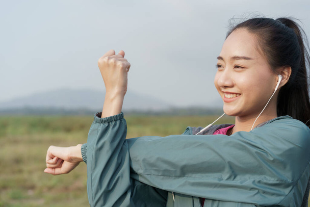 Medium Close- up Asian girl smile on the face, sports women preparing for a workout at outdoor on mountain background in the summer, Woman stretching arms or warming-up, Concept exercise wellness - Foto, imagen