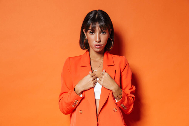 Portrait of a beautiful young brown short haired woman wearing suit standing over orange background, posing - Valokuva, kuva