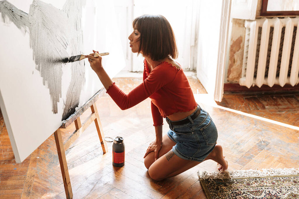 Portrait of young caucasian artistic woman using painting tools while drawing picture in studio - Foto, Bild