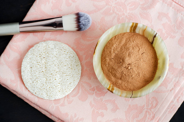 Red cosmetic clay powder in the small onyx bowl, make up brush and loofah sponge. Homemade beauty mask (wrap) for skin and hair. Top view. - Φωτογραφία, εικόνα