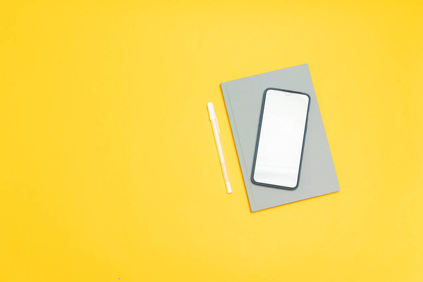 Horní pohled na šablonu smartphonu s prázdnou obrazovkou a šedým notebookem na žlutém pozadí - Fotografie, Obrázek