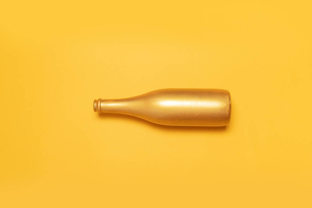 Draufsicht auf die geöffnete goldene Champagnerflasche auf gelbem Hintergrund. Feiertags-Minimalzusammensetzung - Foto, Bild