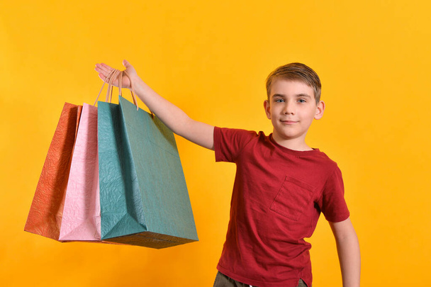Το αγόρι σήκωσε το χέρι του με σακούλες για ψώνια. Χαρούμενος και ευτυχισμένος αγοραστής.. - Φωτογραφία, εικόνα