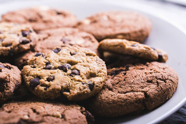 A closeup shot of a lot of chocolate chip cookies in a white plate - 写真・画像