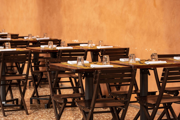 Bolonia, típica mesa de restaurante al aire libre (bajo una columnata) con mantel de papel, cubiertos, vasos y servilletas blancas. Emilia-Romaña, Italia, Europa
 - Foto, Imagen
