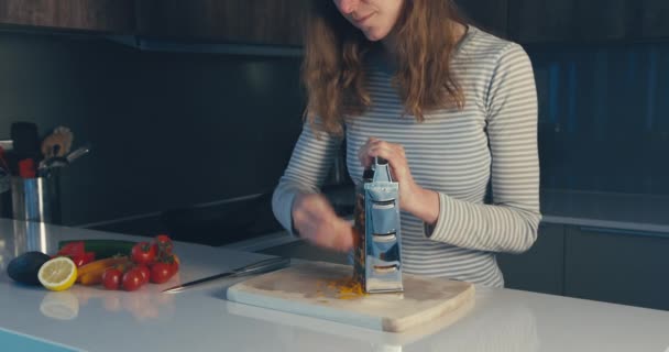 Woman grating carrots with boyfriend in background - Кадры, видео