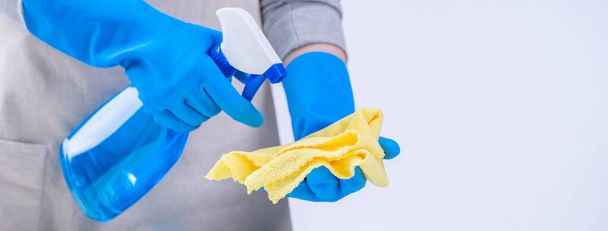 Jonge vrouw huishoudster is bezig met het schoonmaken van witte tafel in schort met blauwe handschoenen, spray cleaner, natte gele doek, close-up, kopieerruimte, leeg ontwerp concept. - Foto, afbeelding