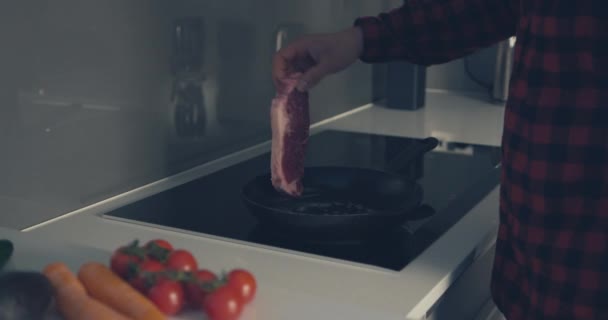 Young man cooking a steak in frying pan - Кадри, відео