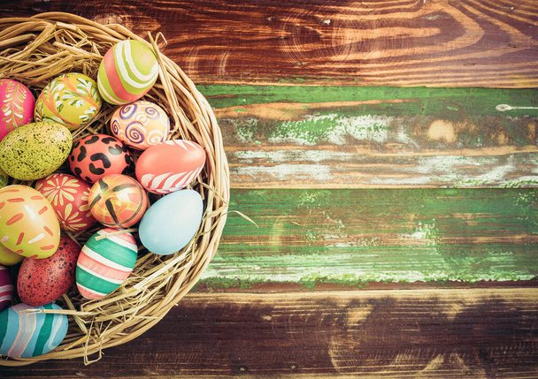 Ovos de Páscoa em vários padrões e cores em um ninho de pássaro colocado em um chão de madeira decorado em estilo retro
. - Foto, Imagem