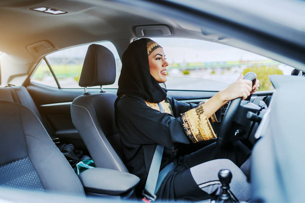 Mladý nádherný usměvavý muslim žena v tradičním oblečení řízení její drahé auto. - Fotografie, Obrázek