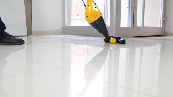 Un uomo che pulisce il pavimento bianco con il aspirapolvere - Foto, immagini