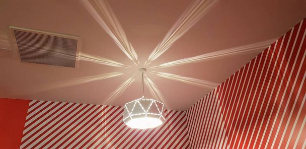 A low angle shot of an illuminated chandelier hanging in a red striped room - Photo, Image