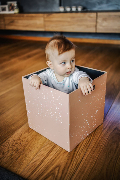 Gyanúsnak tűnő kis szőke fiú ül a dobozban, és félrenéz. Lakberendezés. - Fotó, kép