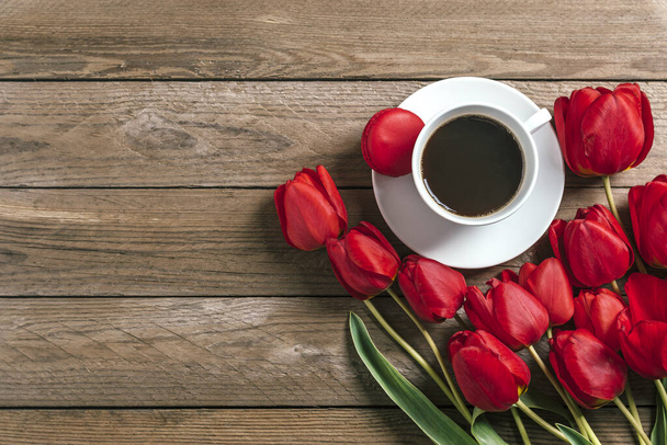 Fila de tulipanes rojos, taza de café negro americano sobre fondo de madera. Espacio para texto, mensaje. Día de las Madres, Hola primavera, buen concepto de la mañana. Tarjeta. Acostado. Vista superior. Estilo rústico
 - Foto, Imagen