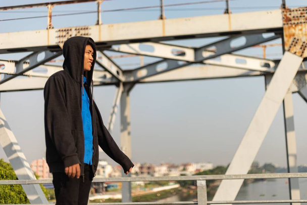 A young Asian man walking on a bridge happily looking ahead - Фото, зображення