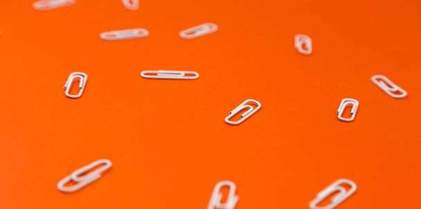 Close-up de clipes de papel branco em um fundo laranja. Padrão de papelaria escolar
 - Foto, Imagem