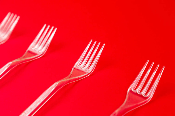 Close-up de garfo de plástico transparente em um fundo vermelho. Padrão de utensílios de mesa descartáveis
. - Foto, Imagem