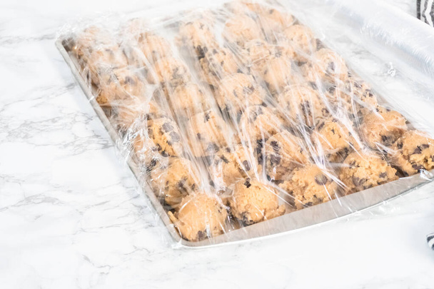 Wrapped chocolate chips cookie dough scoops on a baking sheet. - Valokuva, kuva
