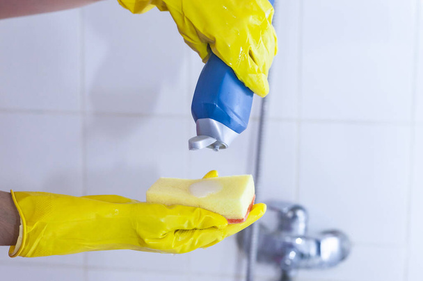 Háziasszony takarítja a fürdőszobai csapot és a zuhanyt. Sárga védőkesztyűs szobalány mossa a piszkos fürdőcsapot. Női kézmosás vagy fürdés tisztítása - Fotó, kép